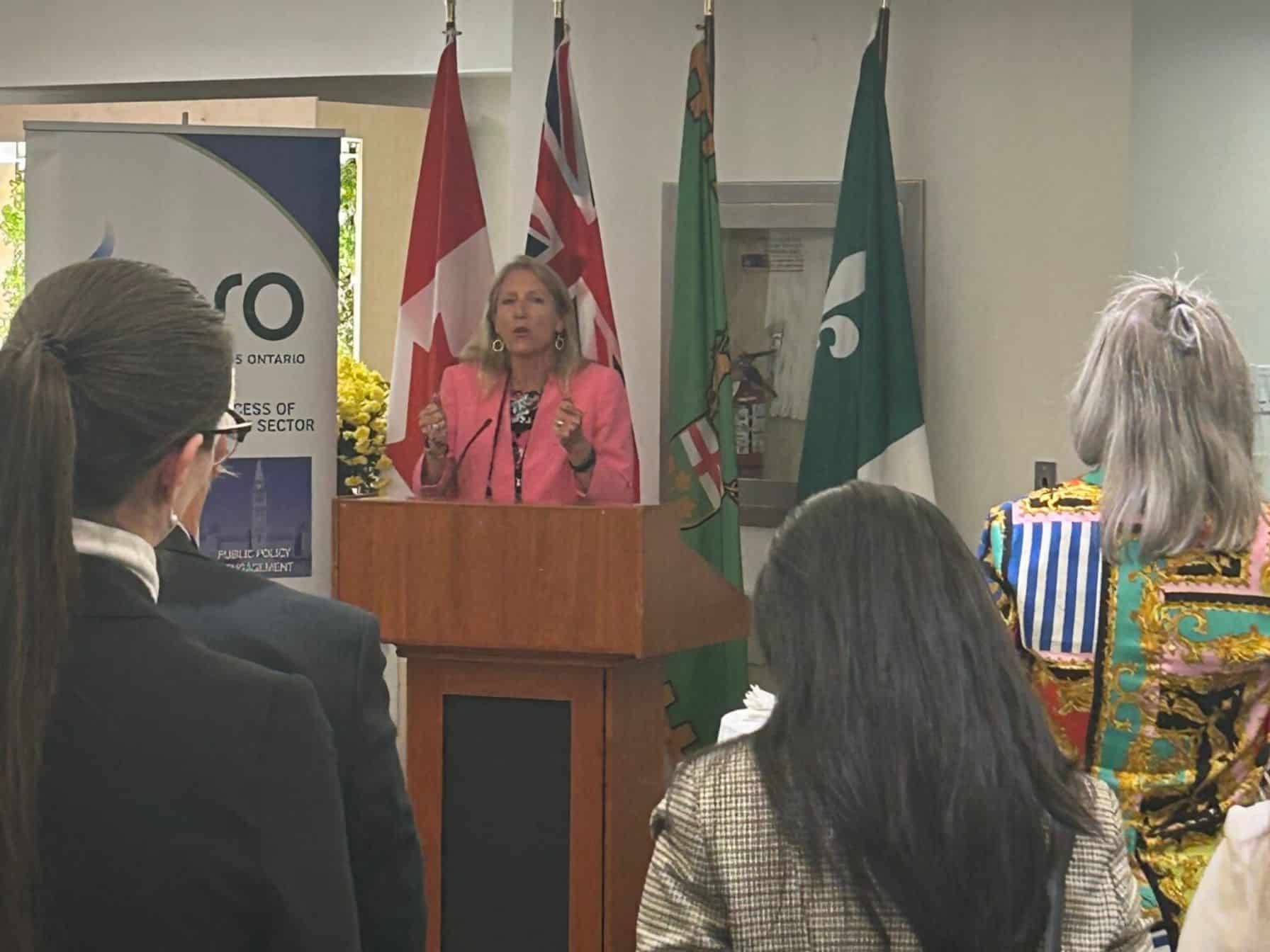 Woman speaking at podium with flags